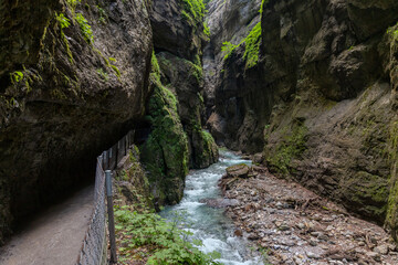 Narrow walkway carved into the cliffside along a turquoise stream inside Partnachklamm Gorge,...