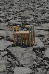 Simple wood chair sitting incongruously on a desolate rocky landscape, appearing out of place and alone.