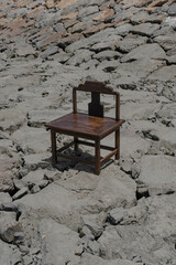 Ornate wooden chair perched on rocky ground, contrasting textures and serene composition of chair and rocks.