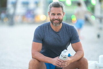 Sport fitness man resting on a bench outdoors. Mature fitness sport model sitting on a bench after...