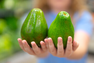 Avocado in kids hand. Healthy fruit for children. Avocado close-up, selective focus on avocado....