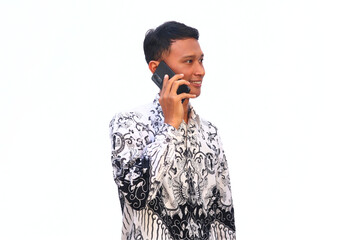 An Asian male teacher wearing a PGRI batik uniform makes a phone call with happy expression