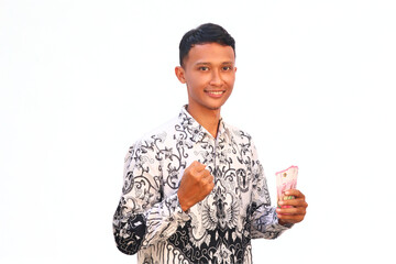 An Asian male teacher wearing a PGRI batik uniform holds money with a happy expression.