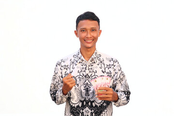 An Asian male teacher wearing a PGRI batik uniform holds money with a happy expression.