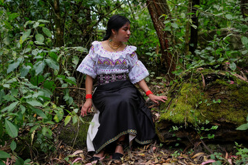Indigenous woman wearing traditional andean clothes sitting on a mossy rock in a lush forest