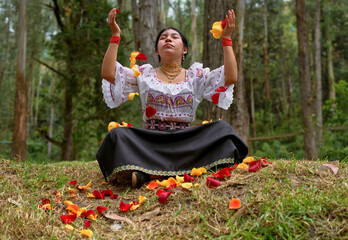 Indigenous woman wearing traditional clothing is sitting in a meditative pose in a forest,...