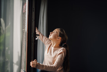 Fototapeta premium Curious girl opening window and looking up in wonder at home