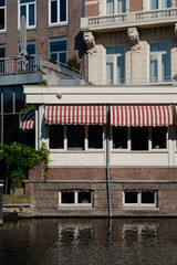 Amsterdam canal-side building with awnings and brick facade reflected in the water.