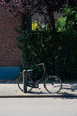 Bicycle propped against a post near a brick wall covered in greenery, creating a charming street scene.