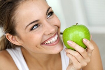 A woman is holding a green apple and smiling