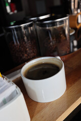 black coffee in the white cup on the wood tray with beans in the jar
