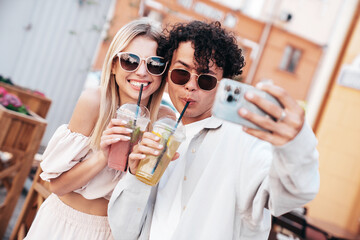 Young smiling beautiful woman and her handsome boyfriend in casual summer clothes. Happy cheerful family. Female having fun. Couple posing in street. Holding and drinking cocktail drink in plastic cup