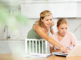 Mom helps her teenage daughter to do her homework and looks carefully at childs notebook. Female...