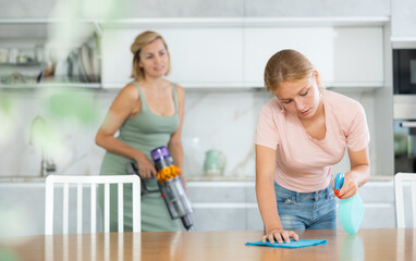 Positive mom and daughter are doing household chores together and chatting casually. Teenage girl...