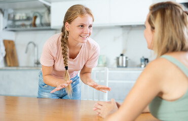 Portrait of cheerful teenage daughter talking friendly to mother in cozy home kitchen. Concept of...