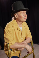 Aged Caucasian man wearing clown makeup and top hat leaning on glittering prop standing on stage...