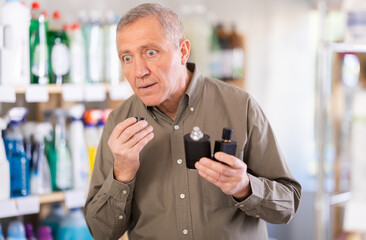 Elderly man standing in a supermarket tastes perfume. Buyer came to the store for a new perfume