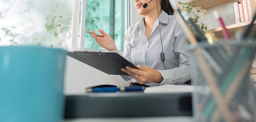 Remote Work. Woman in headset presenting ideas with clipboard in home office.