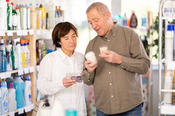 Couple elderly man and woman buyers chooses scented candles in household chemicals store