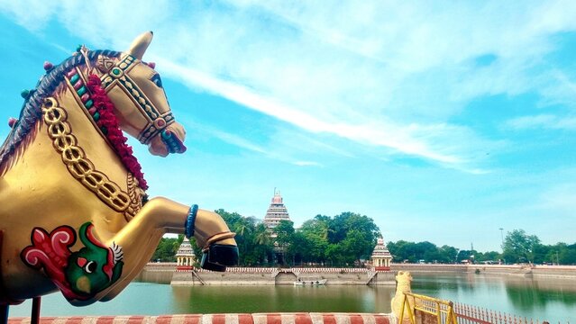 Madurai, Tamilnadu, India - August 8 2025: A vibrant horse statue stands near the Mariamman Theppakulam tank in Madurai, with the Meenakshi Amman Temple mandapam visible across the sacred water