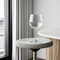 A close-up shot reveals an empty wine glass delicately placed on a stylish grey bar stool in a modern, minimalist interior setting near a large window with city views.