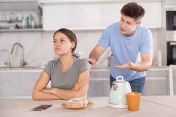 Apologetic boyfriend trying to apologize after quarrel and calm down upset young girl sitting at...
