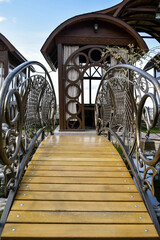 Small bridge with black ornate wrought-iron railings on background of summer gazebo. Close-up.