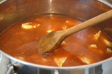 Chopped chicken breast pieces cooking as stew in a pot, close-up kitchen view.