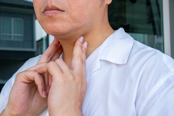 Fototapeta premium Close-up of hand pressing sore throat against a blurred background, illustrating tracheal discomfort and respiratory distress. Ideal for throat and airway treatment ads.