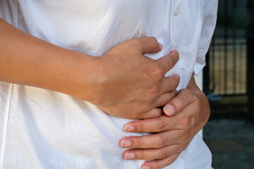 Close-up of a hand clutching the abdomen against a neutral backdrop, highlighting gastrointestinal...