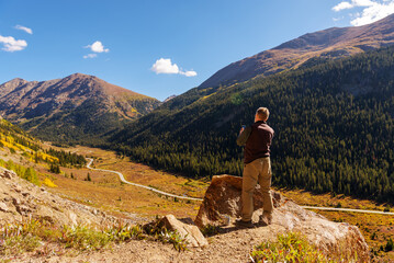 On a colorful fall road trip through Colorado, a male tourist takes pictures of the scenic...