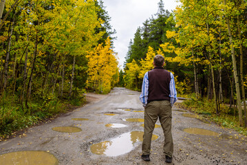 Obraz premium Gray Skies, Golden Aspens: Autumn at in Colorado. A male tourist stands on the rugged road, surrounded by the vibrant colors of fall.