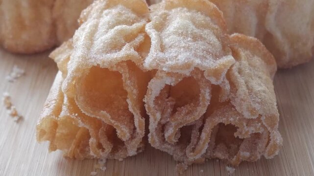 Zoom out reveals a golden Spanish sweet, Flor Frita, resting on a wooden board dusted with sugar.