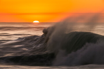 A powerful wave crashes in motion as the sun rises over the horizon at Bronte Beach, Sydney,...