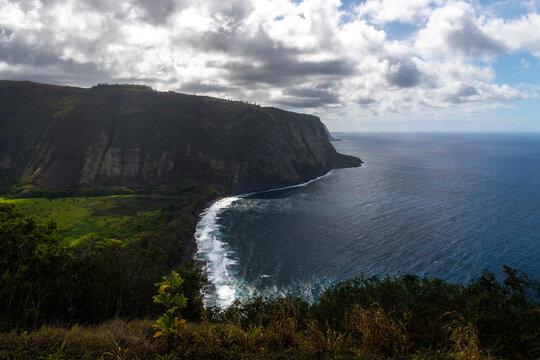 A view of the lush Waipiʻo Valley, with its dramatic cliffs and a winding river leading to a black sand beach on the Big Island of Hawaii, showcasing its natural beauty.