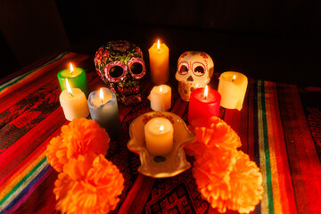 Ceramic skulls with metallic decorations and flowers among colorful candles and magnolias on altar...
