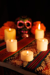 Black skull with metallic floral details and candles on colorful altar honoring the Day of the Dead