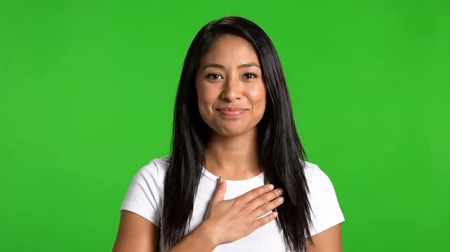 Woman with hand over heart smiles wearing white tshirt green background