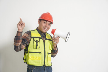 Asian construction worker wearing safety vest and helmet, holding a megaphone and pointing forward, promoting with energy and enthusiasm. Isolated image on white background