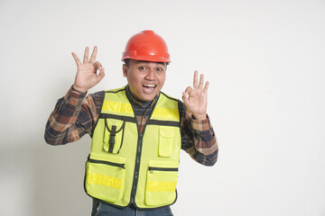 Asian construction worker wearing safety vest and helmet showing ok hand gesture and smiling...