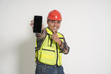 Asian construction worker wearing safety vest and helmet showing blank screen mobile phone mockup while pointing and presenting product. Social media concept. Isolated image on white background