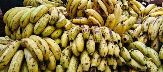 Close-up shot of a large pile of ripe yellow bananas on a market stall. The bananas are arranged in...