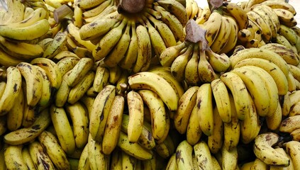 Close-up shot of a large pile of ripe yellow bananas on a market stall. The bananas are arranged in...