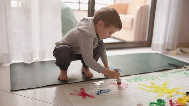Young child painting on floor with colorful tempera