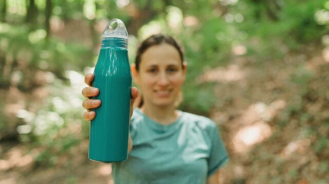 A woman enjoys staying hydrated outdoors with a stylish water bottle in a lush green natural environment