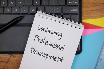 Notebook with Continuing Professional Development Text on Office Desk Scene. with keyboard and office equipment background