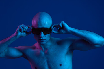 Bold man wearing sunglasses poses under vibrant blue light, showcasing his confidence and...