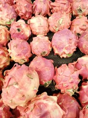 A collection of fresh dragon fruits with vibrant pink and green spiky skins arranged in a retail...