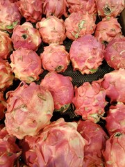 A collection of fresh dragon fruits with vibrant pink and green spiky skins arranged in a retail...