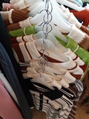 A vertical row of sweaters and knitwear hang on white plastic hangers, with a chain link connecting them, showcasing various colors and ribbed textures